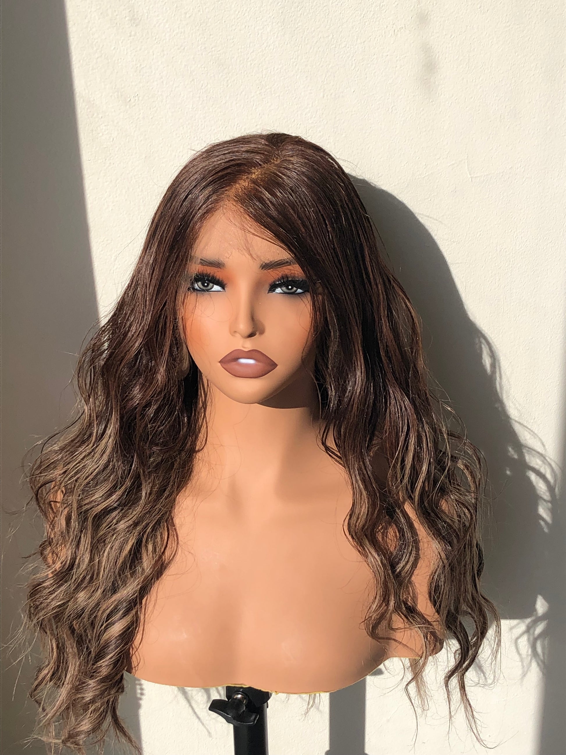 Mannequin head with long wavy brown wig on a neutral background